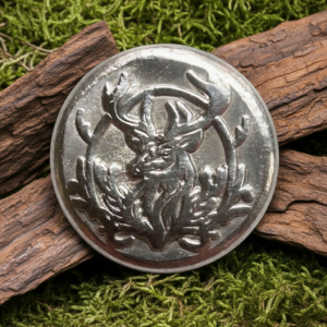 A circular silver round with a detailed stag head embossing, nestled between two pieces of weathered wood on a bed of vibrant green moss.